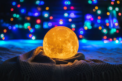 Close-up of illuminated moon crystal lamp on textile against defocused light