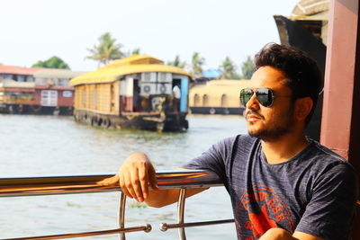 Portrait of young man wearing sunglasses while sitting at harbor