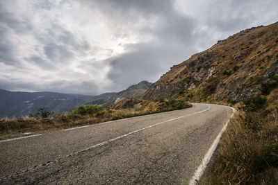 Empty road leading towards mountains against cloudy sky