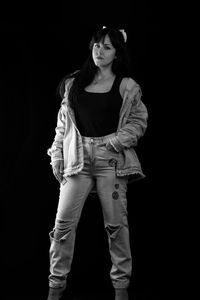 Portrait of young woman standing against black background