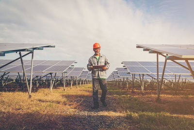 Male electrician walking amidst solar panels on field