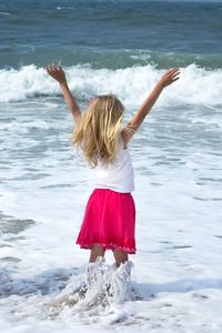 Rear view of girl with arms raised while standing at beach