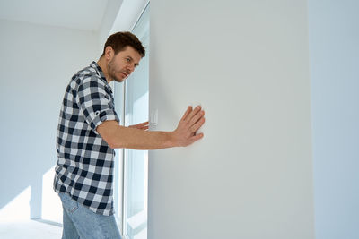Side view of man using digital tablet while standing against wall