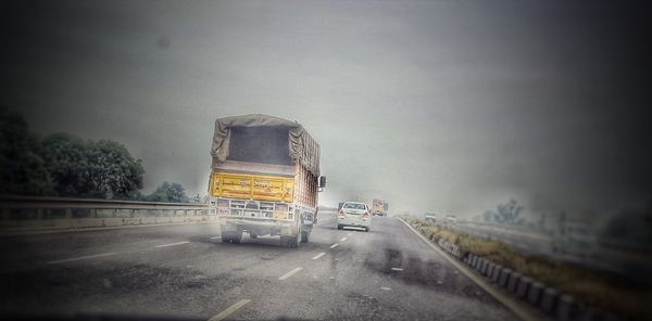Vehicles on road against sky during foggy weather