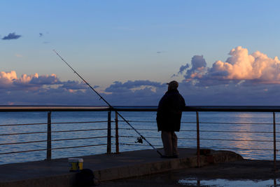 Rear view of man fishing on sea against sky