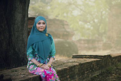 Beautiful woman wearing hijab sitting on retaining wall