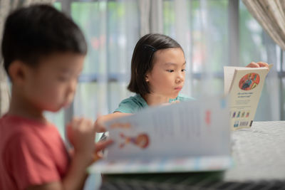 Siblings reading books on table at home