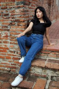 Portrait of young woman sitting against brick wall