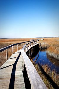 Pier over water amidst dry grass against clear sky