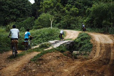 Rear view of people riding bicycle on dirt road in forest