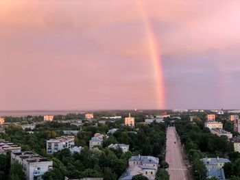 Rainbow over buildings in city against sky at sunset