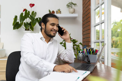 Young man using phone while sitting on table