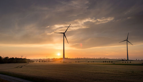 Wind turbines on field against sky during sunset