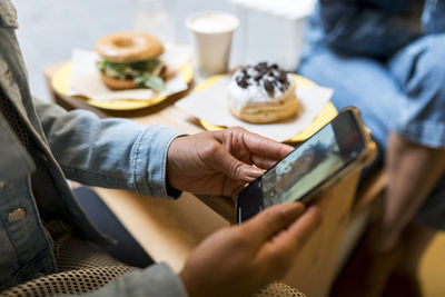 Mid adult woman using mobile phone while sitting with friend at cafe