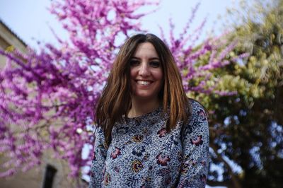 Portrait of smiling young woman standing against purple flowering plants