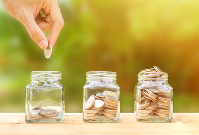 Cropped hand putting coin in jar on table