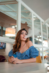 Portrait of young woman looking away while sitting on table