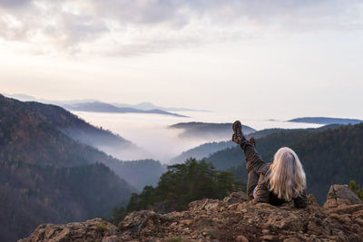 Woman hiker on a mountain top looking low clouds and hills breaking through