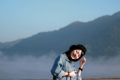 Portrait of smiling woman standing by railing against mountains