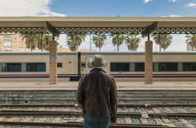Rear view of adult man on cowboy hat waiting in train station.
