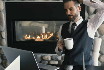 Businessman having coffee while using laptop at home