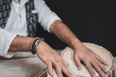 Midsection of man playing tabla against black background