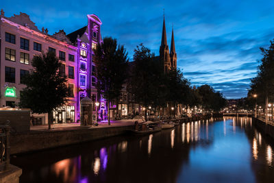 Illuminated building and de krijtberg church by singel canal against cloudy sky