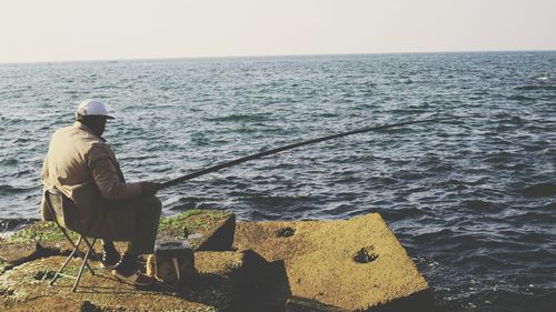 Rear view of man sitting on beach against sky