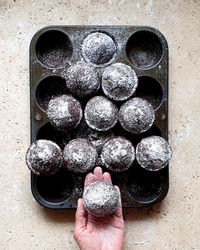 Directly above shot of hand holding cupcake over baking tray on stone table