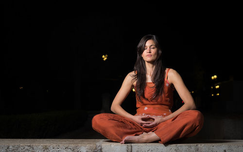 Portrait of young woman sitting against black background