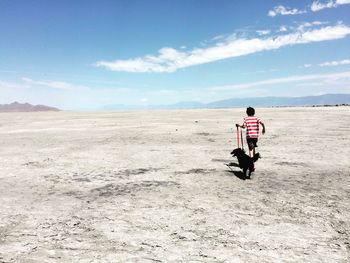 Rear view of boy running with dog on salt flats against sky
