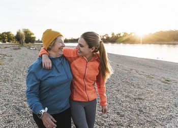 Fit grandmother and granddaughter walking at the river with arms around, having fun