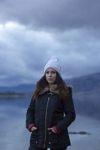 Beautiful woman looking away while standing by lake against sky