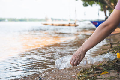 Cropped hand of woman picking plastic bottle from shore at beach