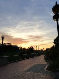 Street by silhouette city against sky during sunset