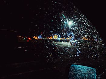 Illuminated city seen through wet car windshield at night