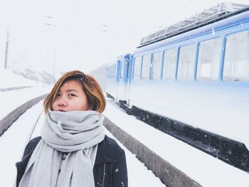Portrait of woman standing against train during snowfall