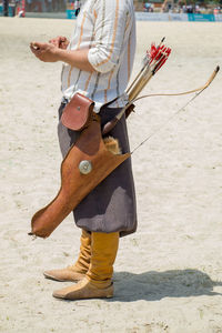 Low section of man with bow and arrow standing at beach