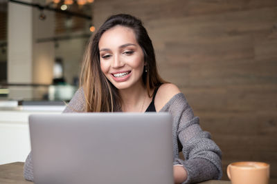 Close-up of smiling young woman using phone while sitting on table