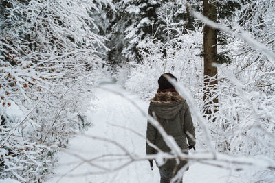 Rear view of woman walking amidst trees during winter