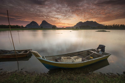 Boats moored in lake against sky during sunset