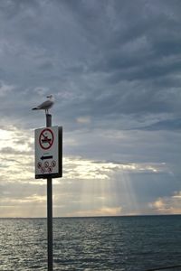 Information sign by sea against sky