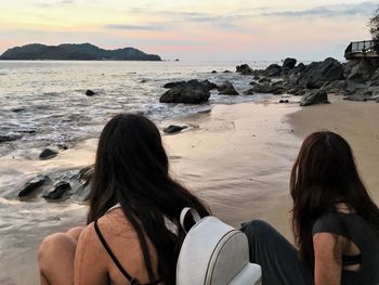 Rear view of people sitting on rock by sea against sky