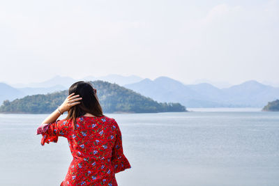 Rear view of woman standing at sea against sky