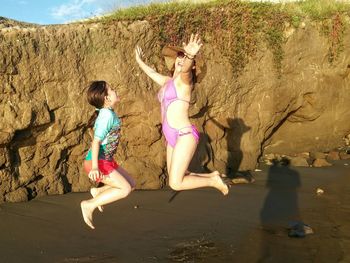 Mother and daughter jumping at beach against rocks