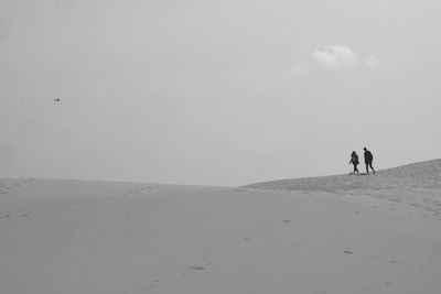 Couple walking at sandy beach against sky