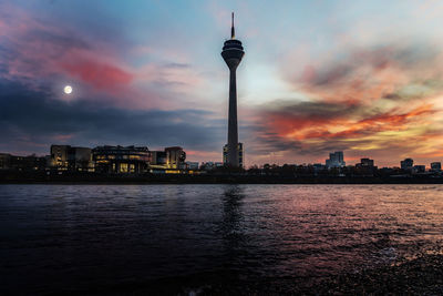 Communications tower in city against sky during sunset