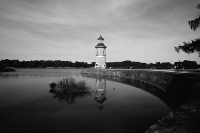 Lighthouse by lake and buildings against sky