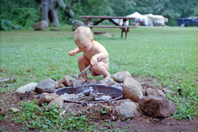 Full length of shirtless boy sitting on field