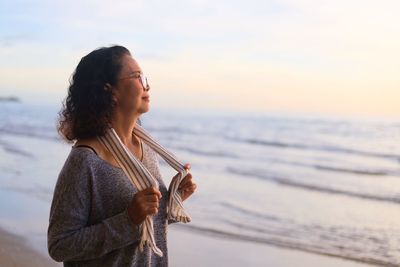 Young woman standing on beach against sky during sunset